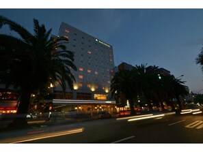 Hotel building with a flat facade and numerous windows, surrounded by palm trees in an urban setting.