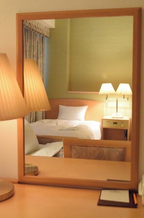 Ein Hotelzimmer mit Bett, Nachttischlampen, einem Nachttisch und einem Spiegel, der den Raum reflektiert.