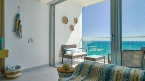 Un balcon avec vue sur l’océan, des meubles en osier et une couverture à rayures.