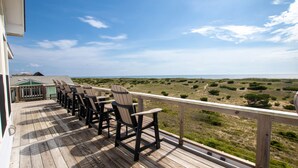 Um deck de madeira com cadeiras Adirondack voltado para a praia.