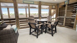 Una terraza de madera con una mesa y sillas, un sofá de mimbre y vista a la playa.