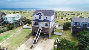 Uma casa de dois andares com varanda frontal, escada que leva ao segundo andar e vista para o oceano.