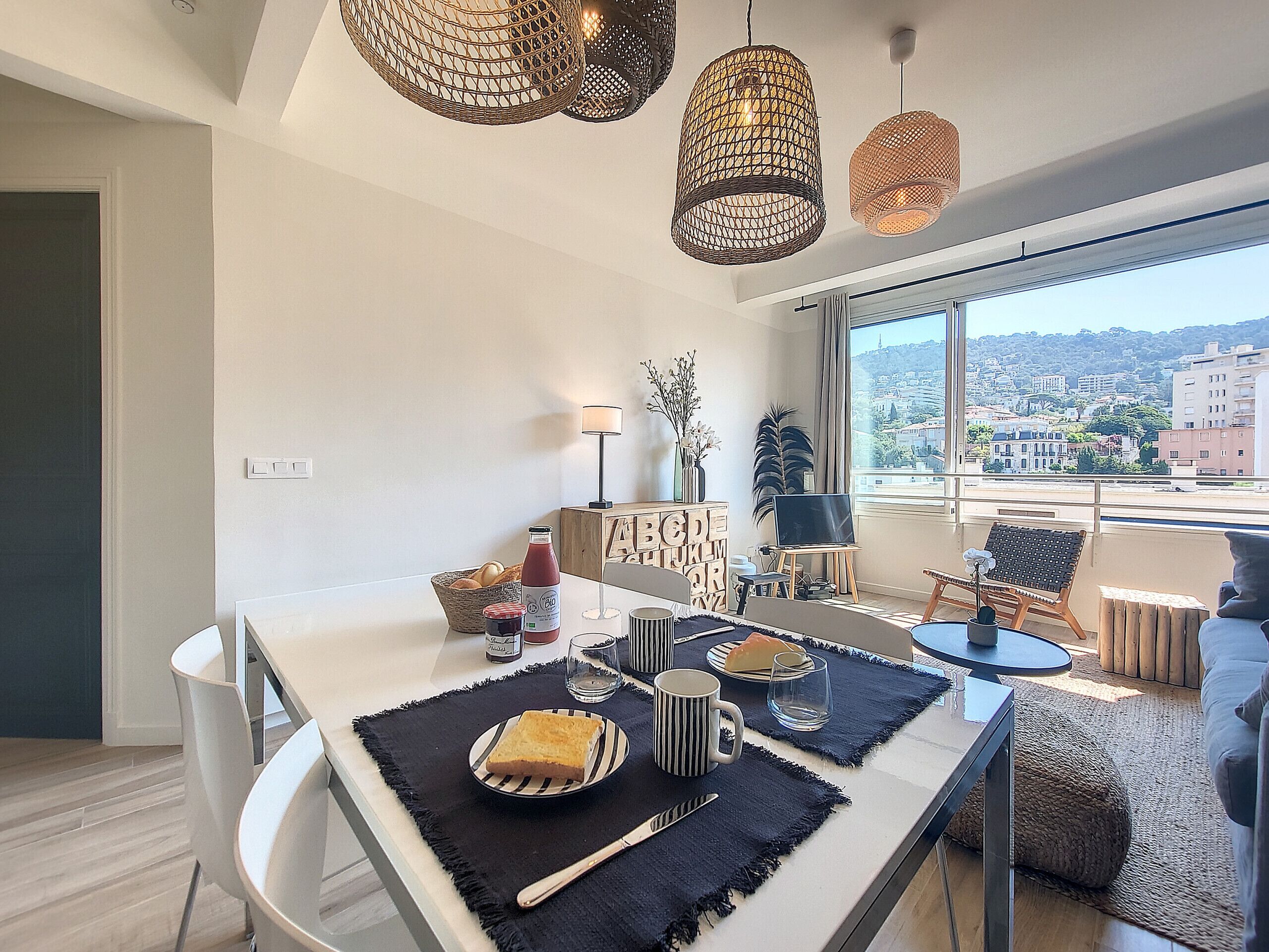 Un espace de restauration moderne avec une table dressée pour deux personnes, une vue sur la ville à travers de grandes fenêtres et des luminaires décoratifs suspendus.