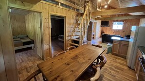 Interno di una baita in legno con tavolo da pranzo, sedie, angolo cottura e soppalco con camera da letto.