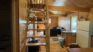 Un interno in legno con una scala centrale, un tavolo da pranzo e un angolo cottura completo di frigorifero e fornello.