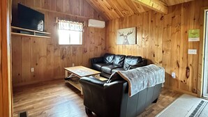 Interno di una baita in legno con un divano, un tavolino e una finestra con tende.