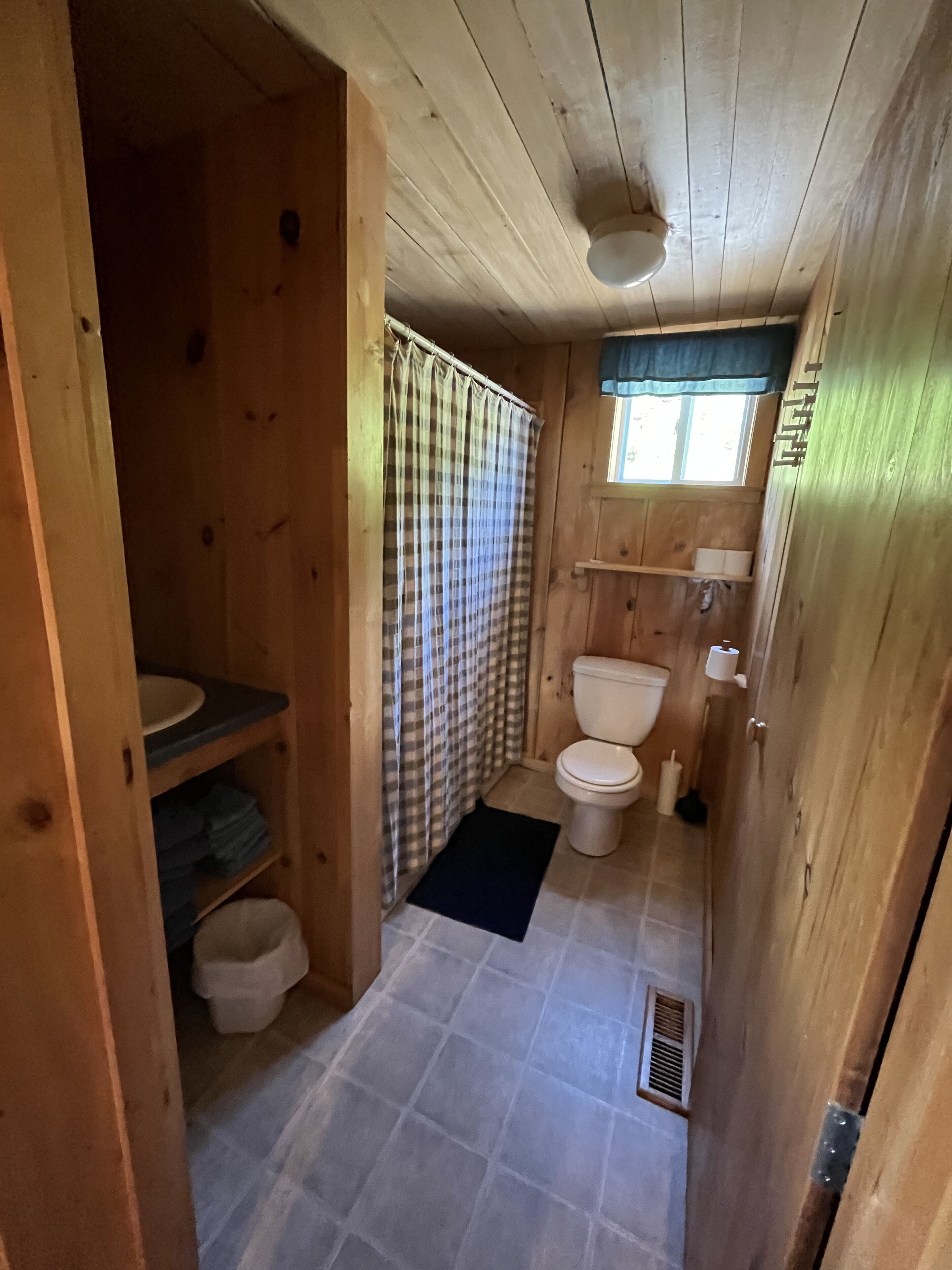 A compact wooden bathroom with a toilet, sink, and shower area.