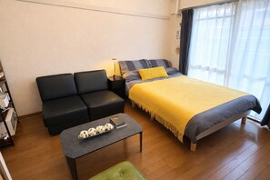 Una camera compatta con un letto, un divano, un tavolino e una sedia verde.