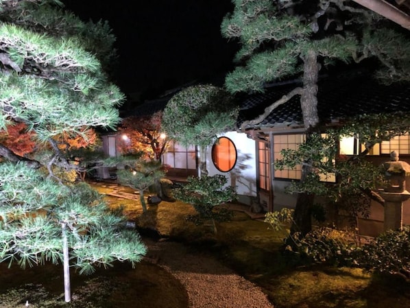 Stroll through a serene traditional Japanese garden surrounded by a variety of trees and a distinctive lantern structure.