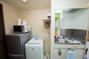 Uma cozinha compacta equipada com frigorífico, micro-ondas e máquina de lavar roupa pequena.