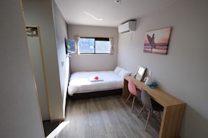Une chambre à coucher de taille modeste, comprenant un lit, un bureau, une chaise, une fenêtre et un climatiseur fixé au mur.