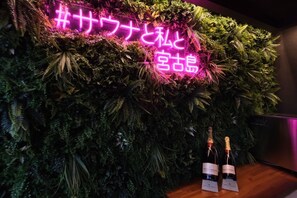Una pared con un letrero de neón y dos botellas de vino sobre una superficie de madera.