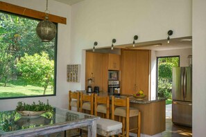 A modern kitchen with wooden cabinets, a built-in island, and a large window overlooking a garden.