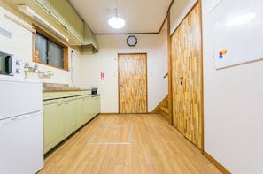 A narrow hallway with wooden flooring, a clock on the wall, and a door with a wooden panel design.