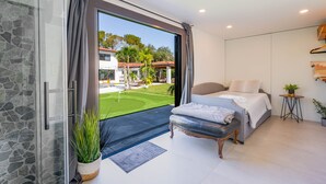 A modern bedroom with a large window, a bed, a small table, and a potted plant. - Villa W/ Pickleball Court, Gym, Sauna & Games! (Miami)