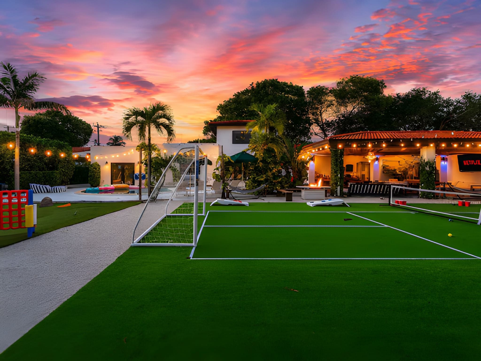 Un court de tennis avec un filet, entouré d’un bâtiment doté d’une terrasse et d’une piscine.
