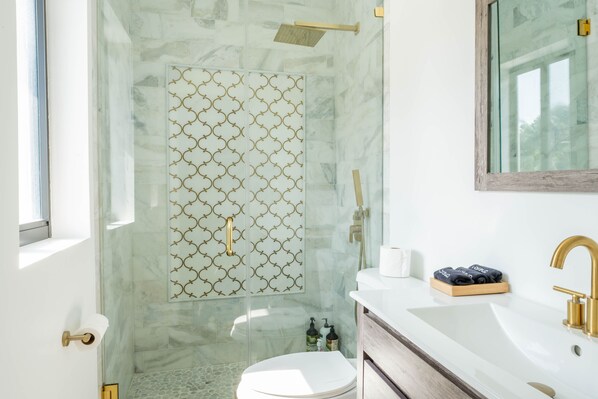 Une salle de bain moderne avec une douche à parois de verre, un lavabo blanc doté de robinetterie dorée et des toilettes.