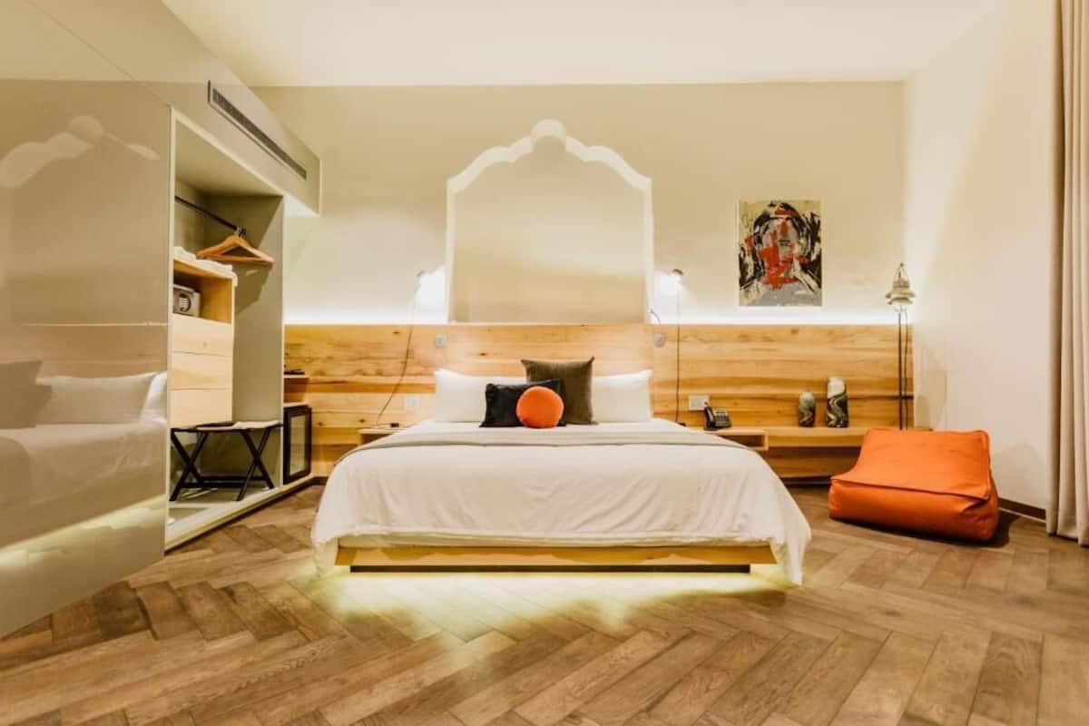 Une chambre à coucher moderne avec un grand lit, une tête de lit en bois, des tables de chevet, un miroir et un tableau accroché au mur.