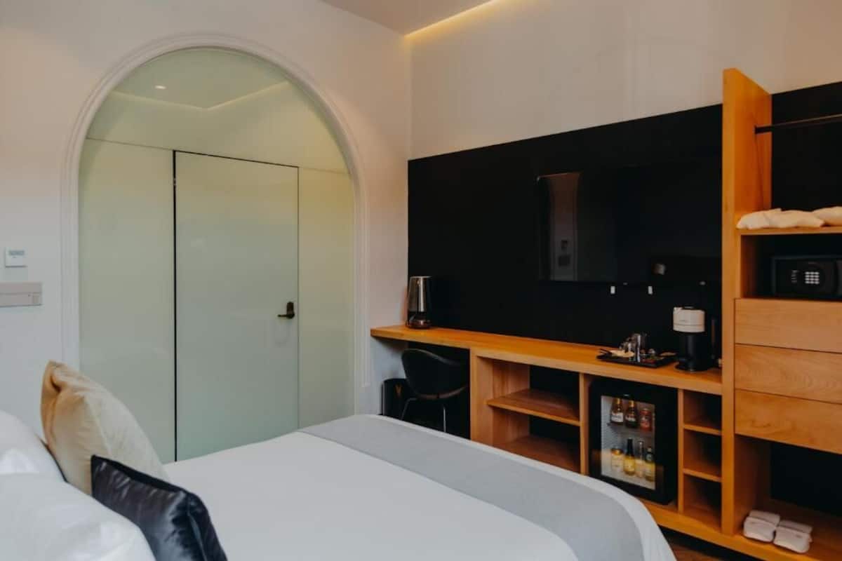Une chambre d’hôtel moderne équipée d’un lit, d’une télévision, d’une machine à café et d’un mini-bar.