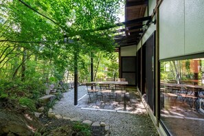 Eine Terrassensitzgruppe mit Tischen und Stühlen, umgeben von Bäumen und einem Kiesweg.