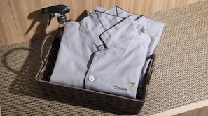 Un cesto di vimini contenente una camicia grigia piegata, con un bottone e un piccolo logo ricamato sul polsino.