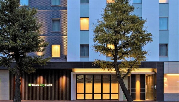 Un hôtel moderne, avec une façade à motifs géométriques, de grandes fenêtres et une enseigne indiquant « Tmark City Hotel ».