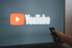 Eine Hand hält eine Fernbedienung vor einem Bildschirm mit dem YouTube-Logo.