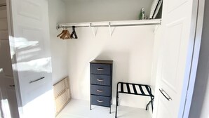 A walk-in closet with a dark-colored dresser, a metal bench, and a clothing rack.