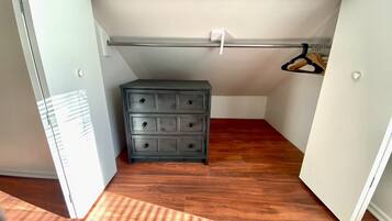 A small, enclosed room with a wooden floor, a gray dresser with multiple drawers, a white ceiling, and a white door.