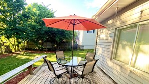 A wooden deck with a glass table and chairs, an umbrella, and a bench.