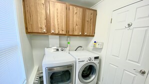 A laundry room with two washing machines, wooden cabinets above, a white door, and a power outlet on the wall. - Cozy Lansing Loft - Pet Friendly - Near MSU (Lansing)