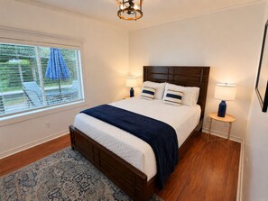 Une chambre à coucher avec un lit en bois, deux lampes de chevet, une fenêtre avec des stores et un tapis à motifs.