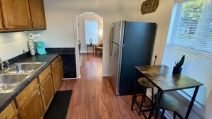 A kitchen with wooden cabinets, a black countertop, a stainless steel sink, a refrigerator, and a small dining area with a table and chairs.