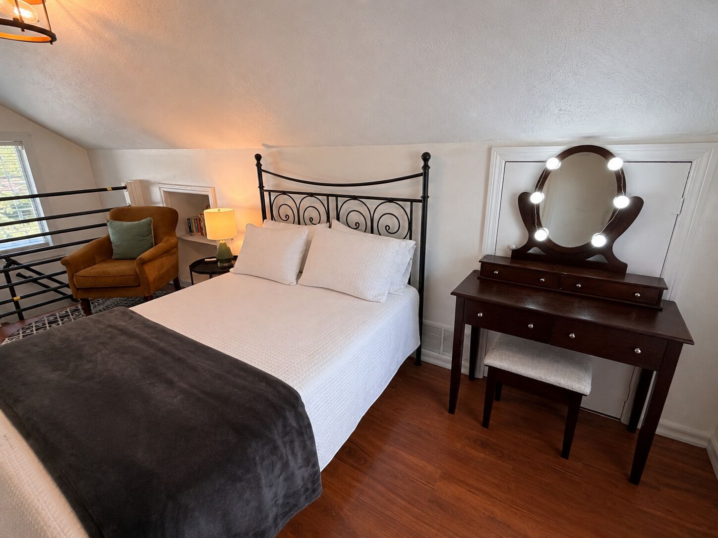 A bedroom with a bed, a vanity with a mirror, a chair, and a lamp.
