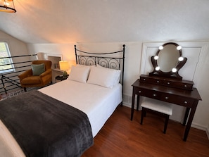 Un dormitorio con una cama, un tocador con espejo, una silla y una lámpara.