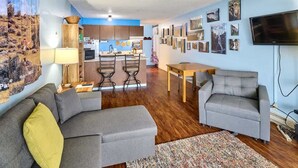 Ein Wohnzimmer mit einer Couch, einem Fernseher und einer Küche im Hintergrund.