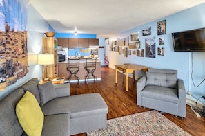 A living room with a sofa, a TV, and a kitchen in the background.