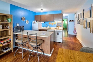 Una cocina compacta con armarios de madera, una isla central con sillas, un microondas y un refrigerador.