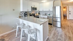 A modern kitchen with white cabinets, a stainless steel refrigerator, and a central island with bar stools. - Ocean View Condo - Second Floor - Pet Friendly! (Lincoln City)