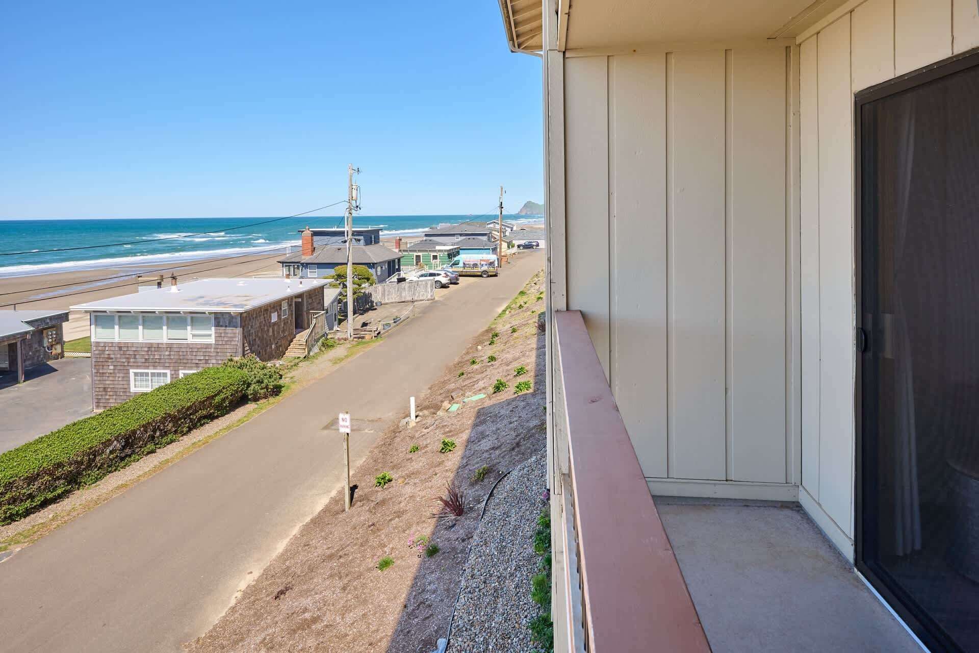A balcony with a view of the beach, a parking area, and a building with a door.