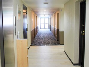 A hotel hallway with a carpeted floor, wooden paneling on the walls, and a door at the end.