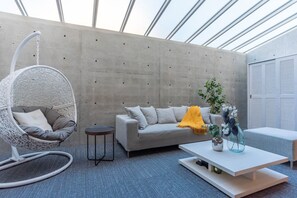 A modern interior with a hanging chair, a sofa, a small table, and a potted plant.