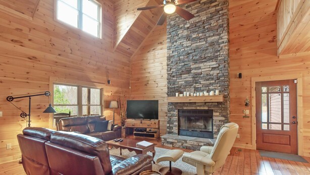 Ein gemütliches Blockhaus-Interieur mit Kamin aus Stein, Ledersofas und einem Fernseher.