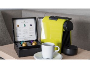 Una máquina de café Nespresso, una caja de cápsulas de café y una taza sobre una mesa.