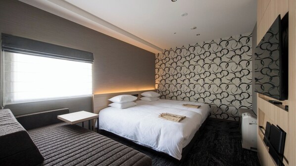 A modern hotel room with a large bed, bedside tables, a flat-screen TV, and a patterned wall.