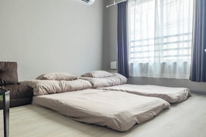 Quarto com cama, almofadas, uma cadeira e janela com cortinas.