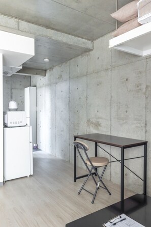 A modern kitchen with a white refrigerator, a microwave, and a small sink. There is a wooden dining table with a chair and a black countertop with a document.