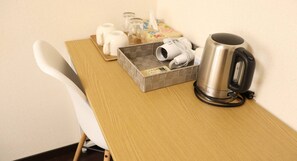 A wooden desk with a kettle, a tray with cups and a tissue box, and a chair.