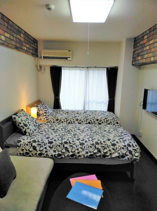 A bedroom with a bed, a bedside table with a lamp, a TV, and a window with curtains.