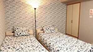 Une chambre avec deux lits, chacun recouvert d’une couvre-lit à motifs floraux, et comprenant une lampe de chevet et une armoire.